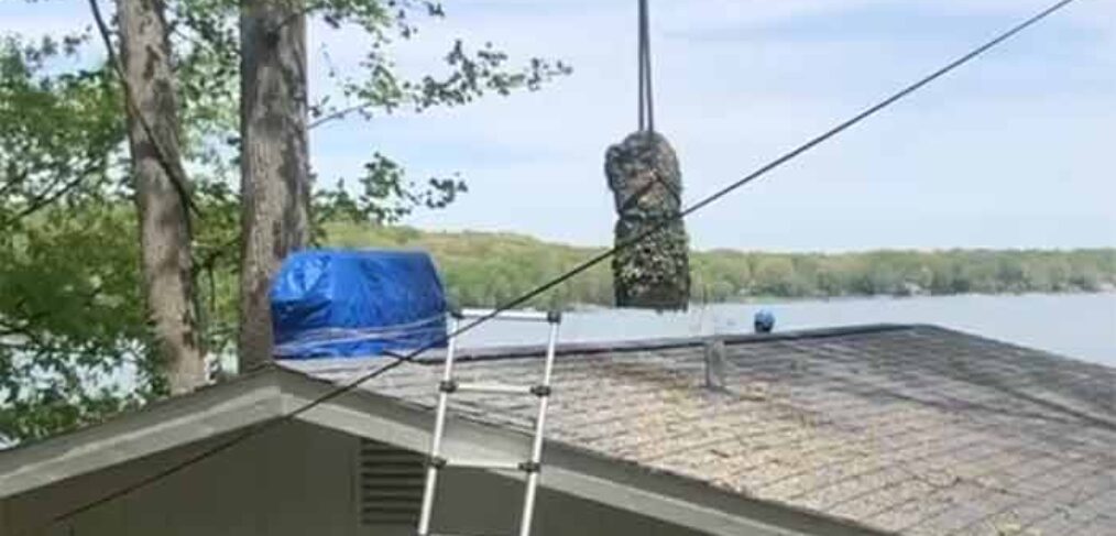 Crane lifting tree trunk section over house roof