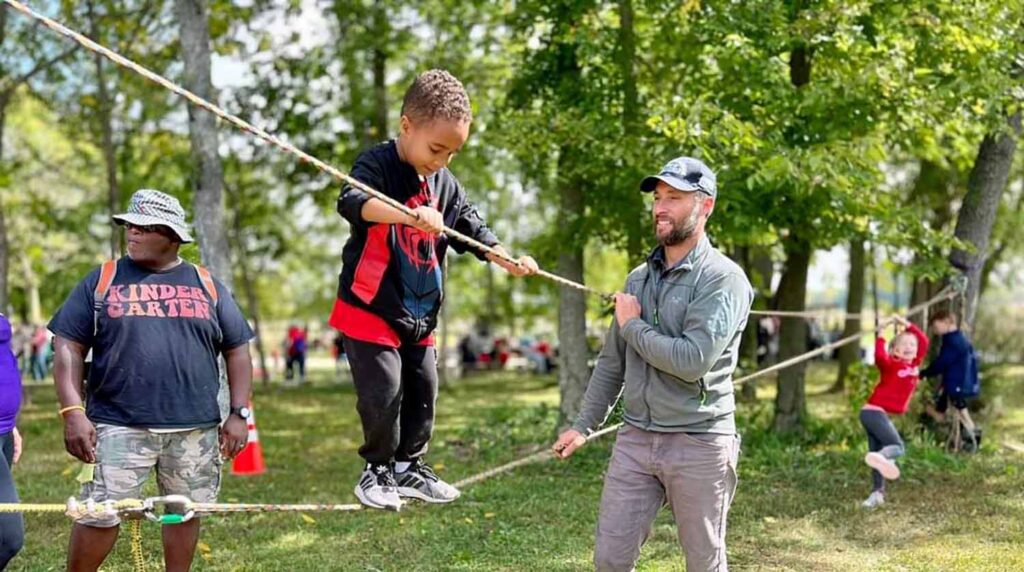 Man and kid crossing a rope bridge between trees in Bloomington, IN