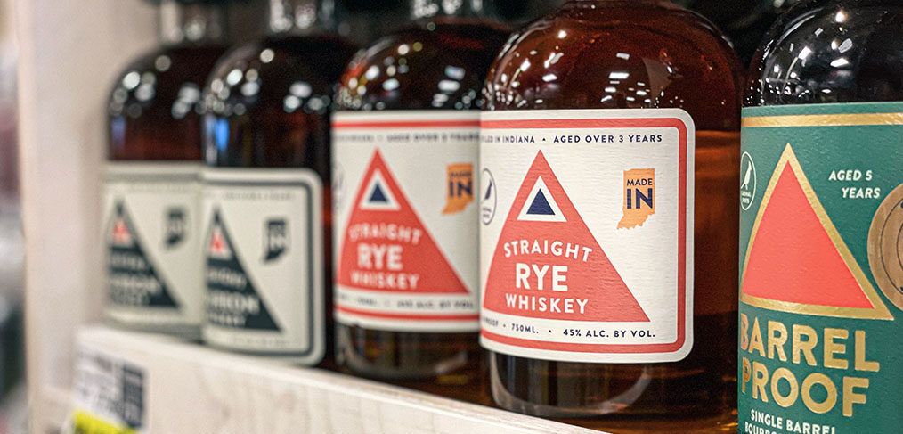 A row of rye whiskey bottles on a wooden shelf in Bloomington, IN