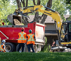 Excavator loading tree debris into a dump truck during residential tree removal